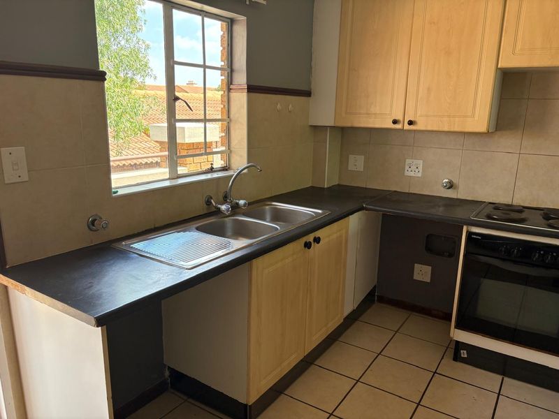 A functional kitchen featuring light wood cabinetry, dark countertops, a double sink, and a built-in electric oven with hob.
