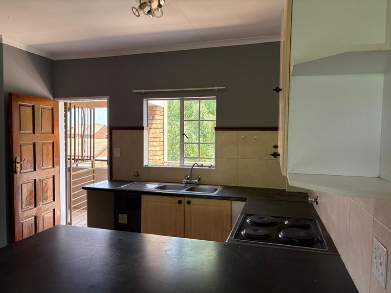 A functional kitchen featuring built-in cabinetry, dark laminate countertops, a double basin sink, and an integrated electric hob with direct access to a balcony.