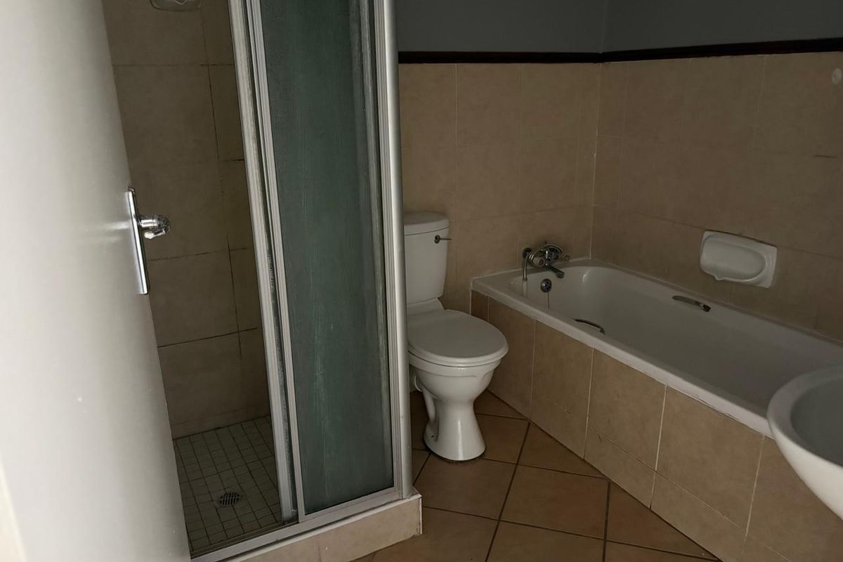 A functional bathroom featuring a separate shower enclosure, a standard bathtub, and a toilet, finished with neutral wall and floor tiling.