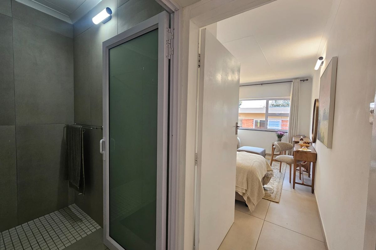 A modern bathroom featuring a walk-in shower with grey tiling, adjacent to a bedroom entrance with neutral floor tiles.