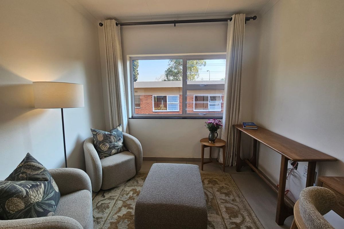 A well-lit living area featuring neutral tiled flooring and a large window with curtain fixtures, providing a comfortable and inviting space.