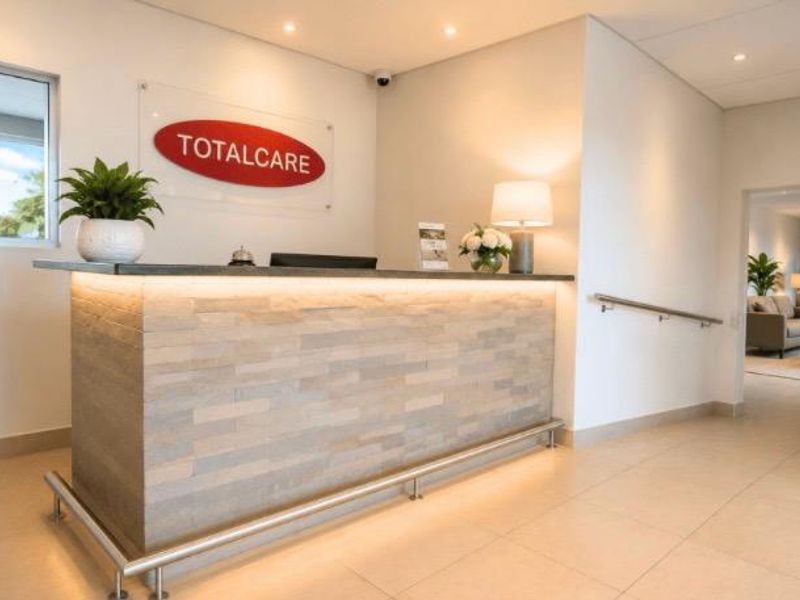 A professional reception area featuring a modern stone-clad desk, integrated lighting, and clean tiled flooring within a well-maintained retirement village facility.