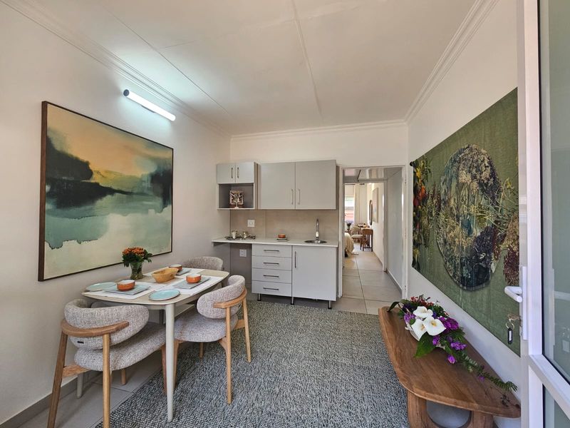 An open-plan living and kitchenette area featuring neutral cabinetry, tiled flooring, and direct access to the adjoining bedroom space.