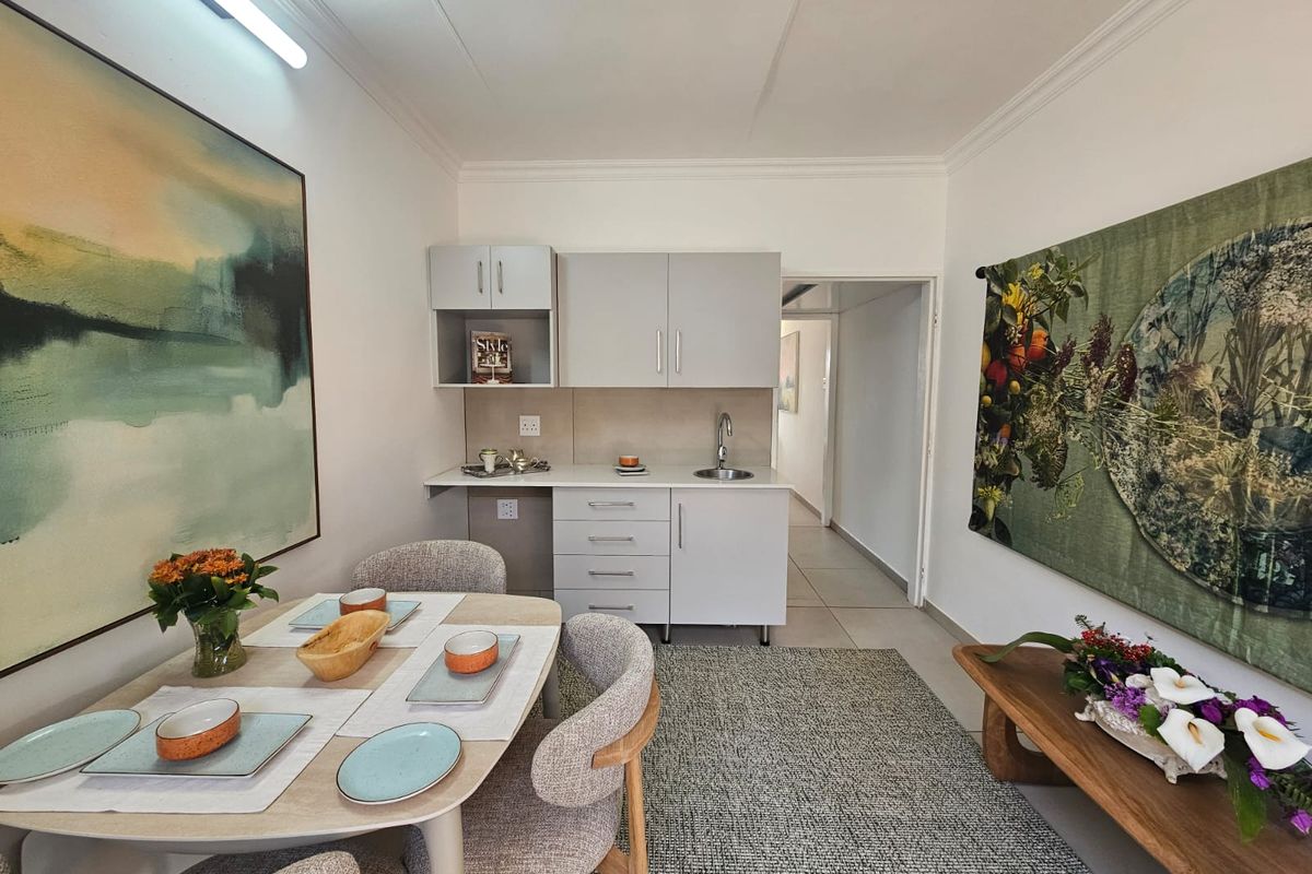 A compact kitchen area featuring modern grey cabinetry, a stainless steel sink, and neutral tiled flooring, seamlessly integrated into the living space.