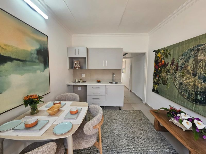A compact kitchen area featuring modern grey cabinetry, a stainless steel sink, and neutral tiled flooring, seamlessly integrated into the living space.