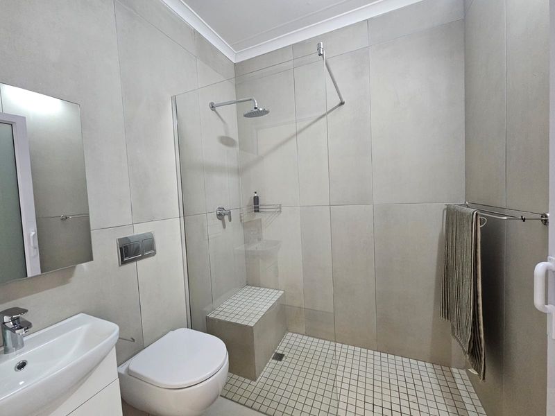Modern bathroom featuring a walk-in shower with a built-in bench, rain shower head, wall-mounted toilet, and a sleek vanity basin.