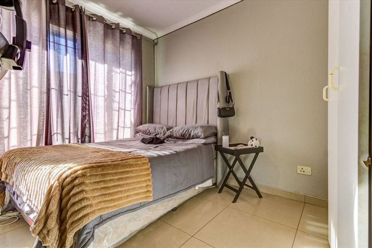 A functional bedroom featuring tiled flooring, a built-in cupboard, and large windows with curtain rails, providing a comfortable and practical living space.