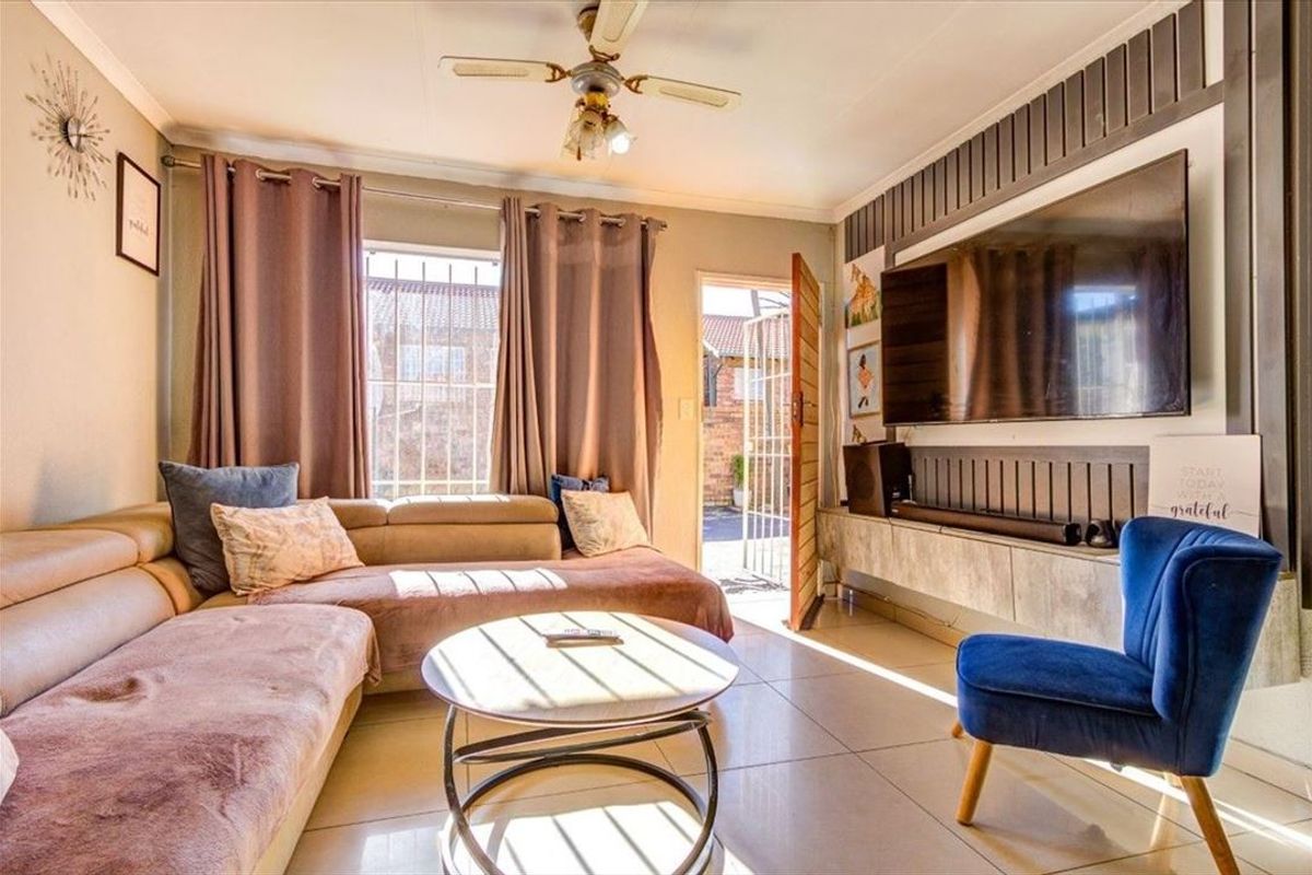 A comfortable living room featuring tiled flooring, a ceiling fan, and a modern built-in media console with decorative slatted wall paneling.