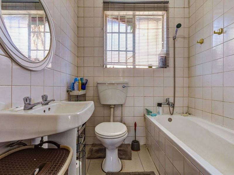 A functional bathroom featuring a pedestal basin, toilet, and bathtub with shower mixer, finished with tiled walls and flooring.