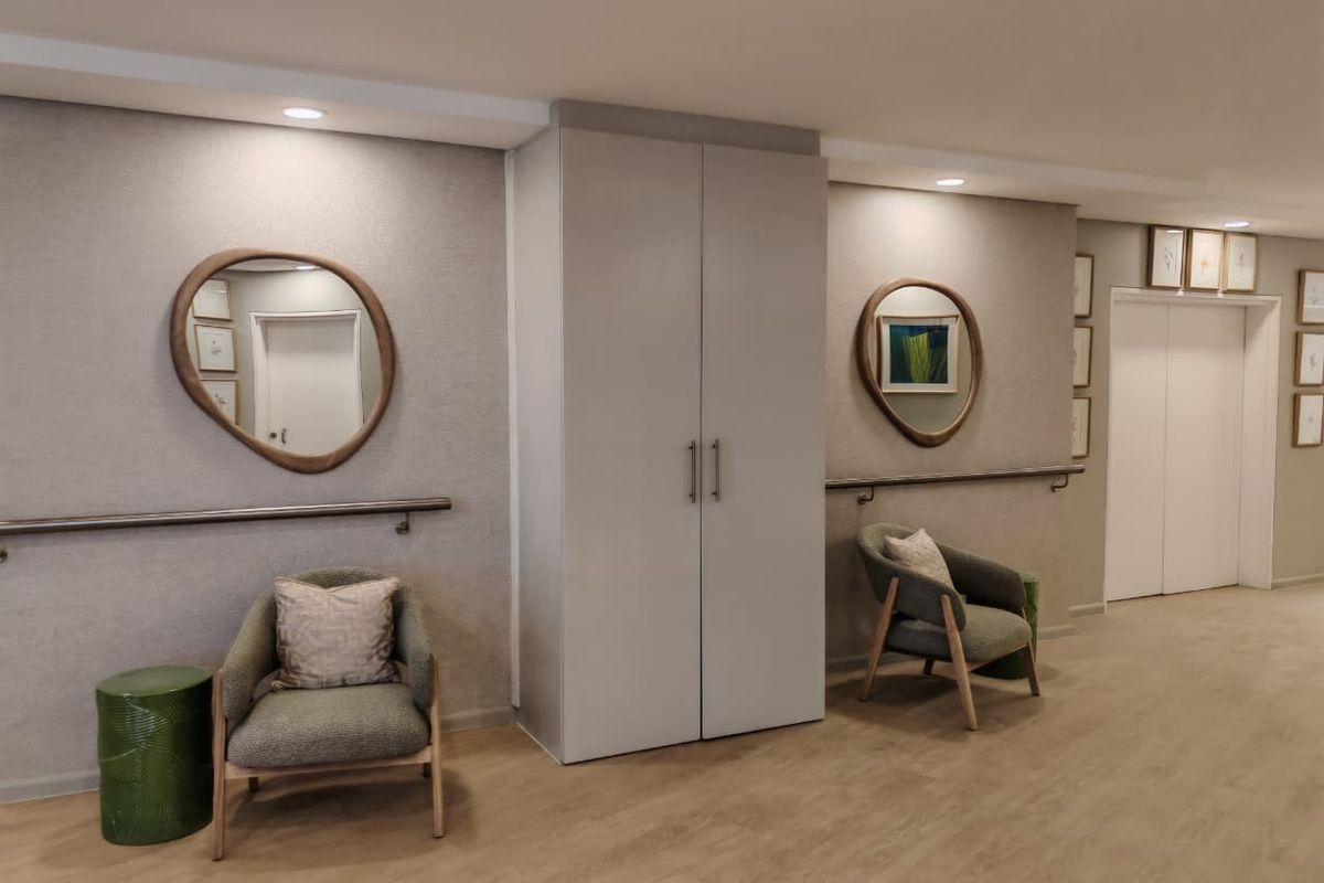 A well-maintained retirement village hallway featuring built-in storage cupboards, wall-mounted safety grab rails, recessed lighting, and access to elevator facilities.