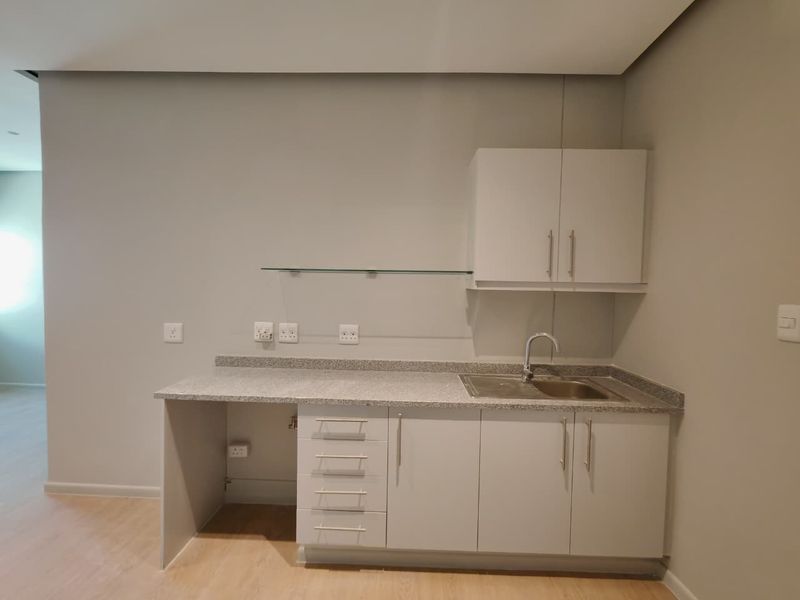 A clean and functional scullery or utility area featuring granite countertops, built-in cabinetry, a stainless steel sink, and a floating glass shelf.