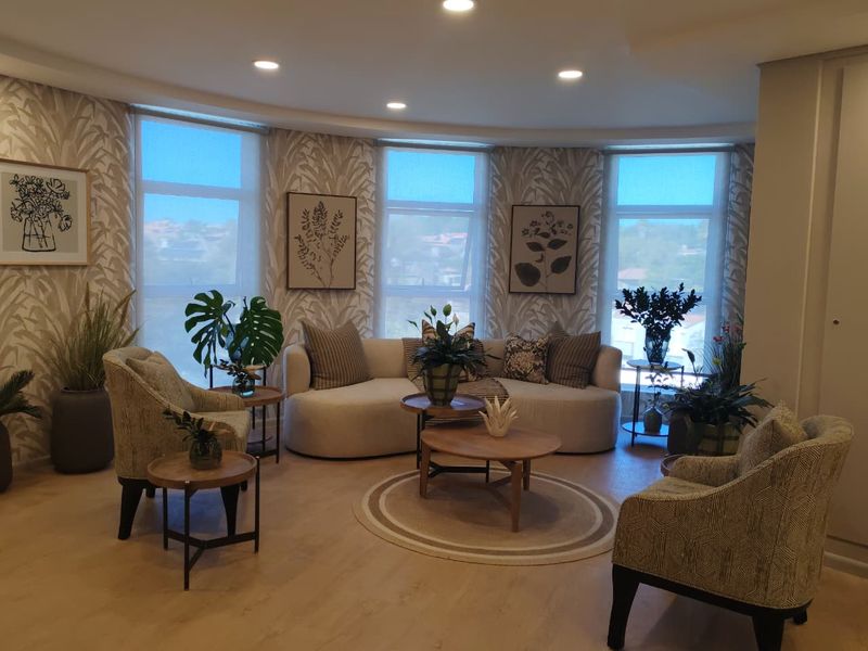 A bright and modern living room featuring a curved window wall, recessed downlighting, and high-quality laminate flooring in a retirement village setting.