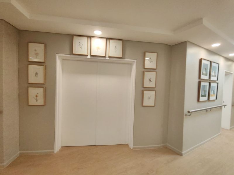 A well-maintained hallway featuring recessed lighting, a safety grab rail, and double doors, finished with neutral wall tones and wood-look flooring.