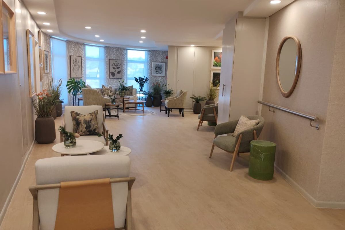 A bright and well-maintained communal living area featuring modern laminate flooring, recessed lighting, and a wall-mounted grab rail for accessibility.