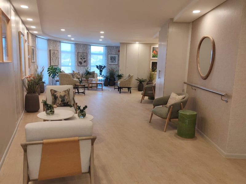 A bright and well-maintained communal living area featuring modern laminate flooring, recessed lighting, and a wall-mounted grab rail for accessibility.