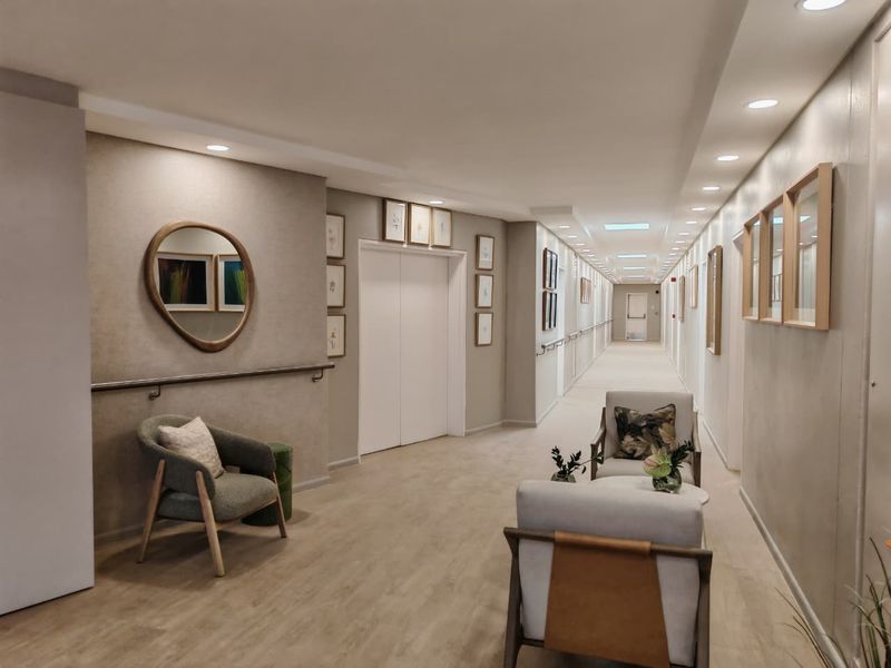 A well-maintained, modern retirement village hallway featuring recessed lighting, grab rails for accessibility, and elevator access.