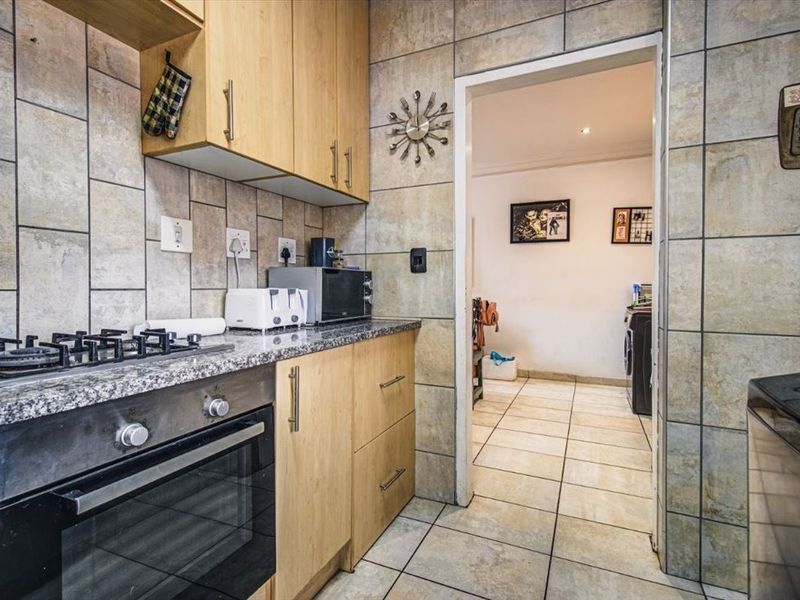 A functional kitchen featuring light wood cabinetry, granite countertops, a built-in gas hob and oven, with tiled walls and flooring throughout.