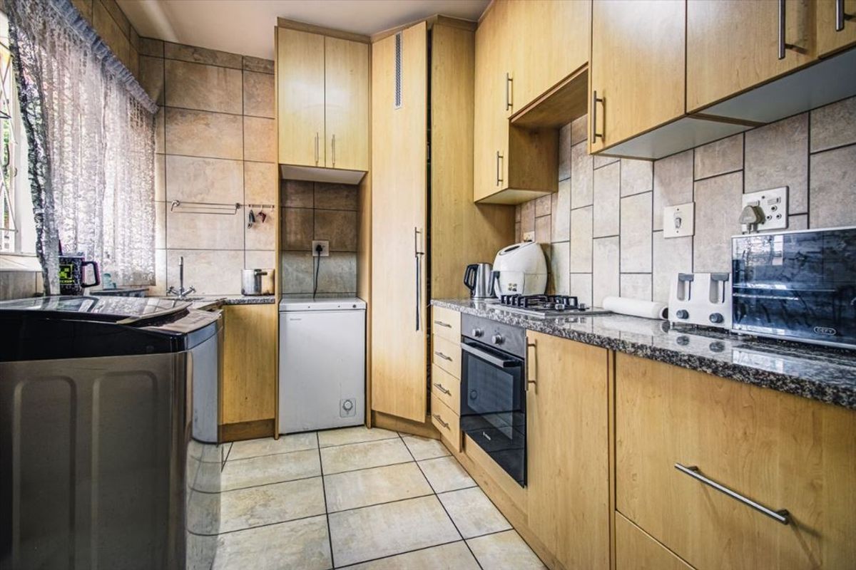 A functional kitchen featuring light wood cabinetry, granite countertops, built-in oven, gas hob, and tiled finishes throughout.