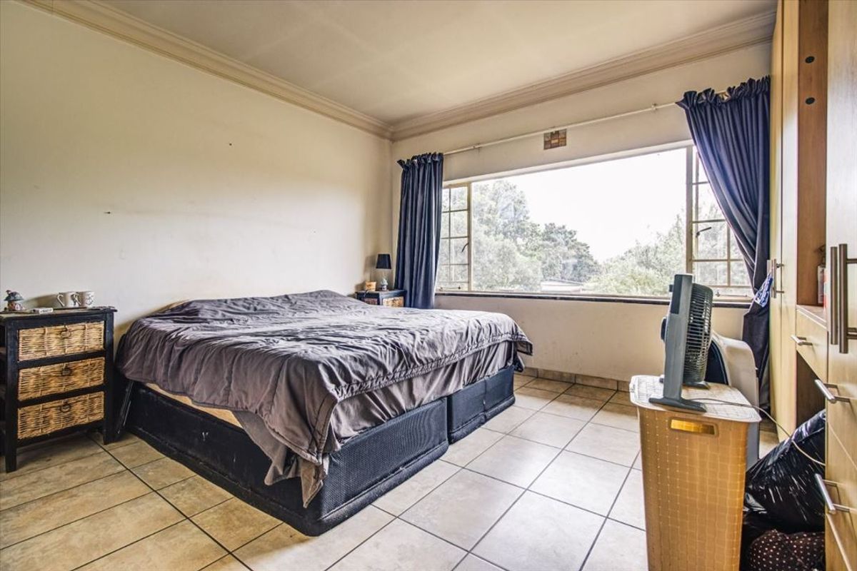 A bedroom featuring tiled flooring, built-in cupboards, and a large window providing natural light and exterior views.