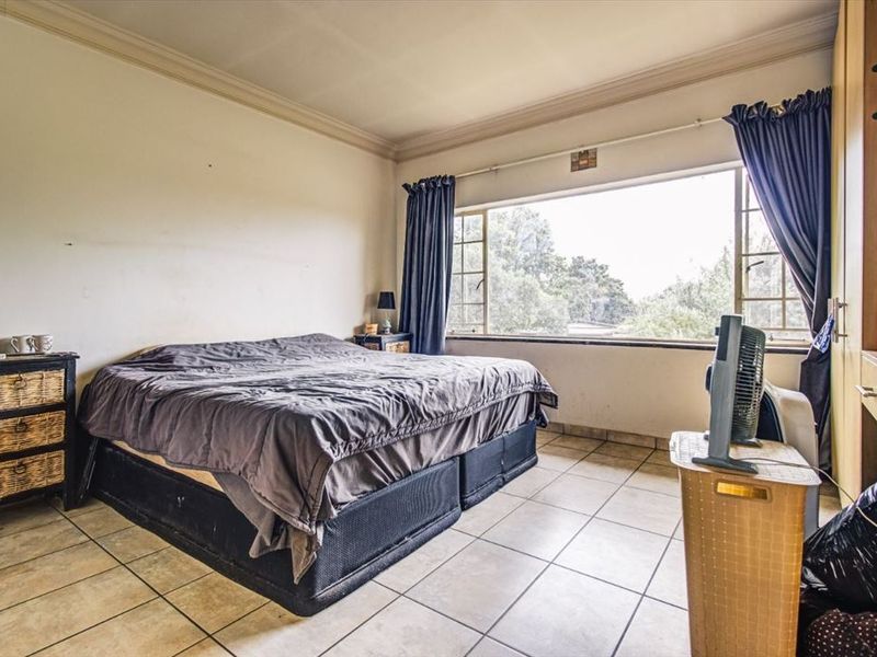 A bedroom featuring tiled flooring, built-in cupboards, and a large window providing natural light and exterior views.