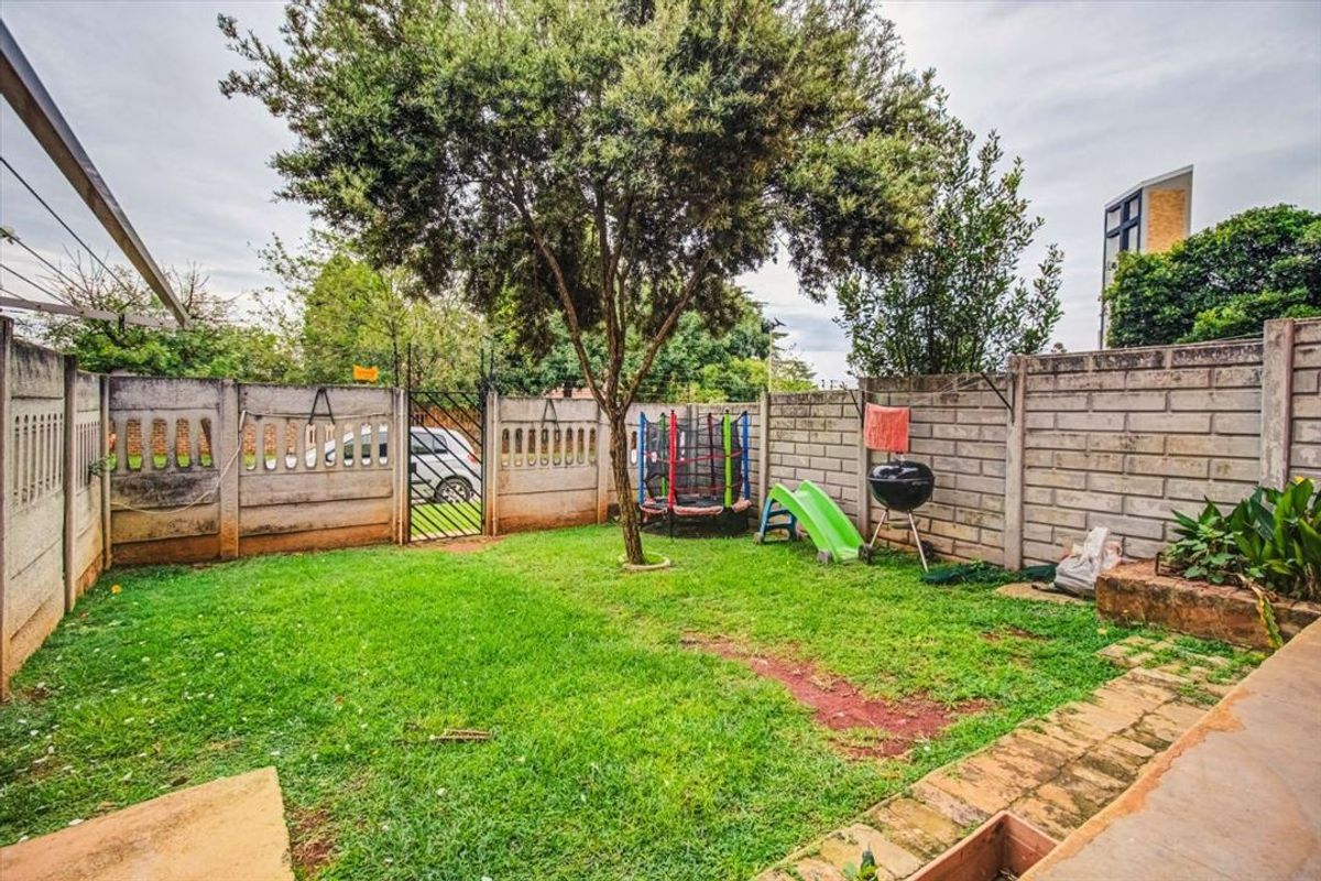 A private rear garden featuring a lawn, mature tree, paved patio area, and secure precast concrete boundary walls with a metal access gate.