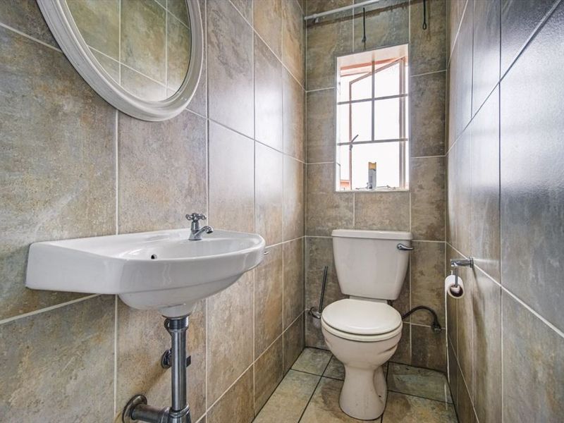 A compact guest bathroom featuring floor-to-ceiling stone-look tiling, a wall-mounted basin, and a standard toilet.