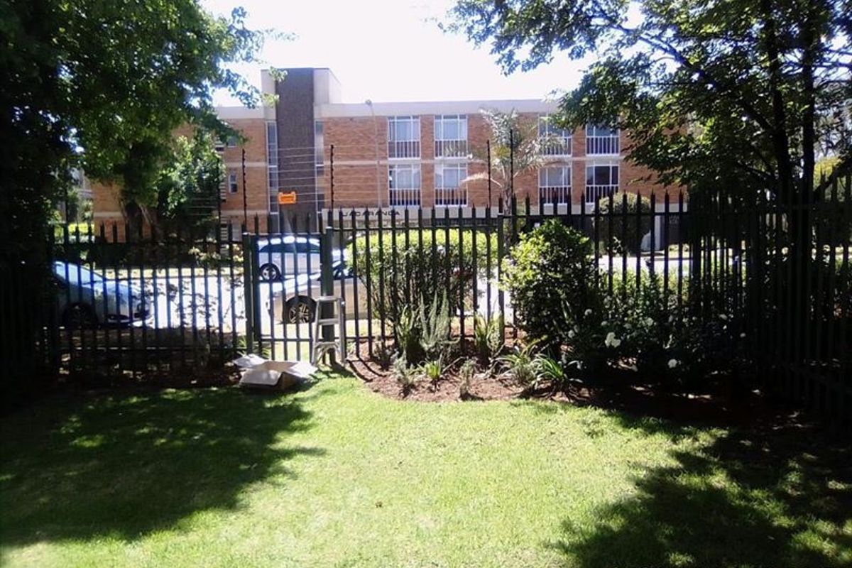A view of the rear garden area featuring established lawn, landscaped garden beds, and secure metal perimeter fencing with electric security wires.