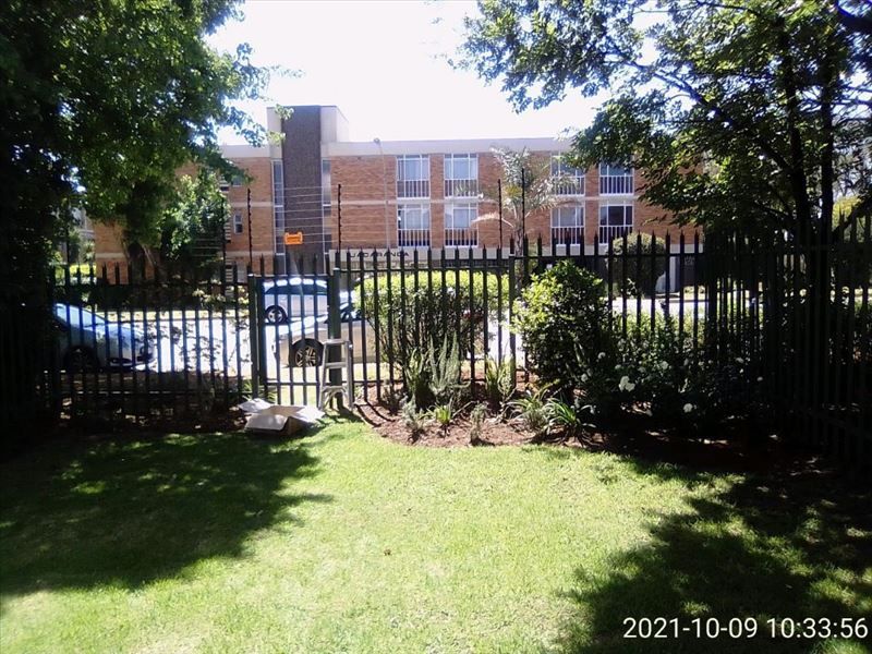 A view of the rear garden area featuring established lawn, landscaped garden beds, and secure metal perimeter fencing with electric security wires.