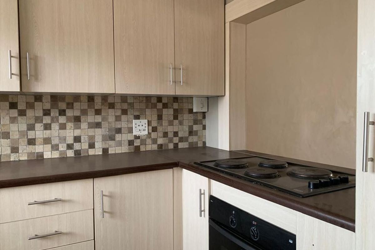 A functional kitchen featuring light wood-look cabinetry, a mosaic tile backsplash, and integrated electric oven and hob.