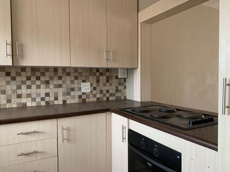 A functional kitchen featuring light wood-look cabinetry, a mosaic tile backsplash, and integrated electric oven and hob.