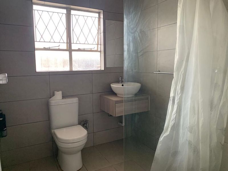 A functional bathroom featuring a wall-mounted vanity with a vessel sink, a toilet, and a glass shower screen with tiled finishes throughout.