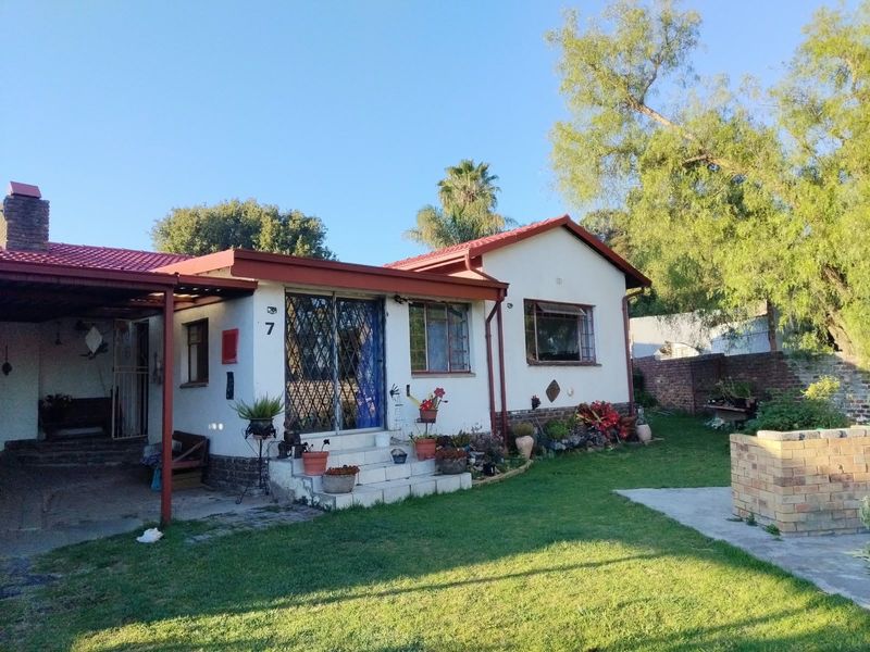 Front view of a single-story house featuring a tiled roof, attached carport, security gates, and a front garden with a brick boundary wall.