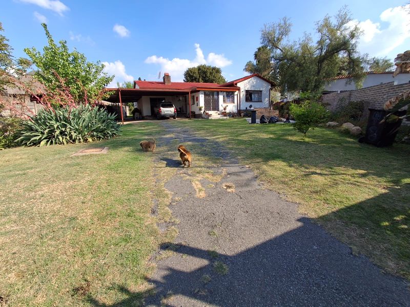 Front view of a single-story house featuring a tiled roof, attached carport, and a long asphalt driveway leading to the entrance.