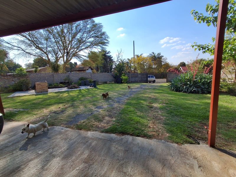 A covered patio area overlooking a spacious backyard with a brick boundary wall, built-in braai, and gated access.