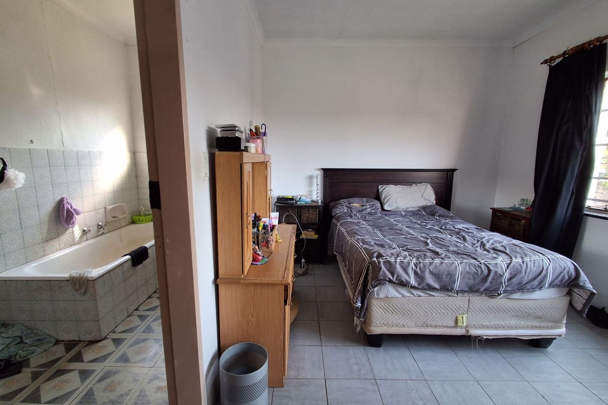 A bedroom featuring tiled flooring with an adjoining bathroom area containing a built-in bathtub and tiled splashback.
