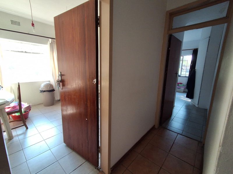 A functional hallway connecting multiple rooms, featuring tiled flooring and traditional wooden doors with a transom window above the entrance.