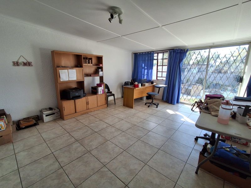 A functional office space featuring tiled flooring, a large sliding glass door with security bars, and direct access to the exterior.