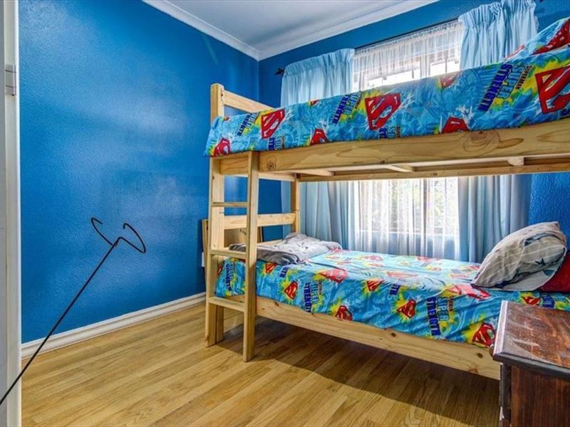 A bedroom featuring laminate flooring and blue painted walls, providing a functional space with natural light from the window.
