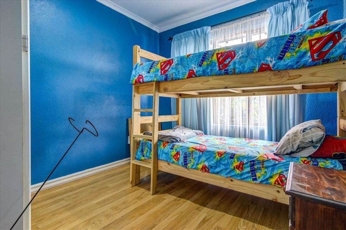 A bedroom featuring laminate flooring and blue painted walls, providing a functional space with natural light from the window.