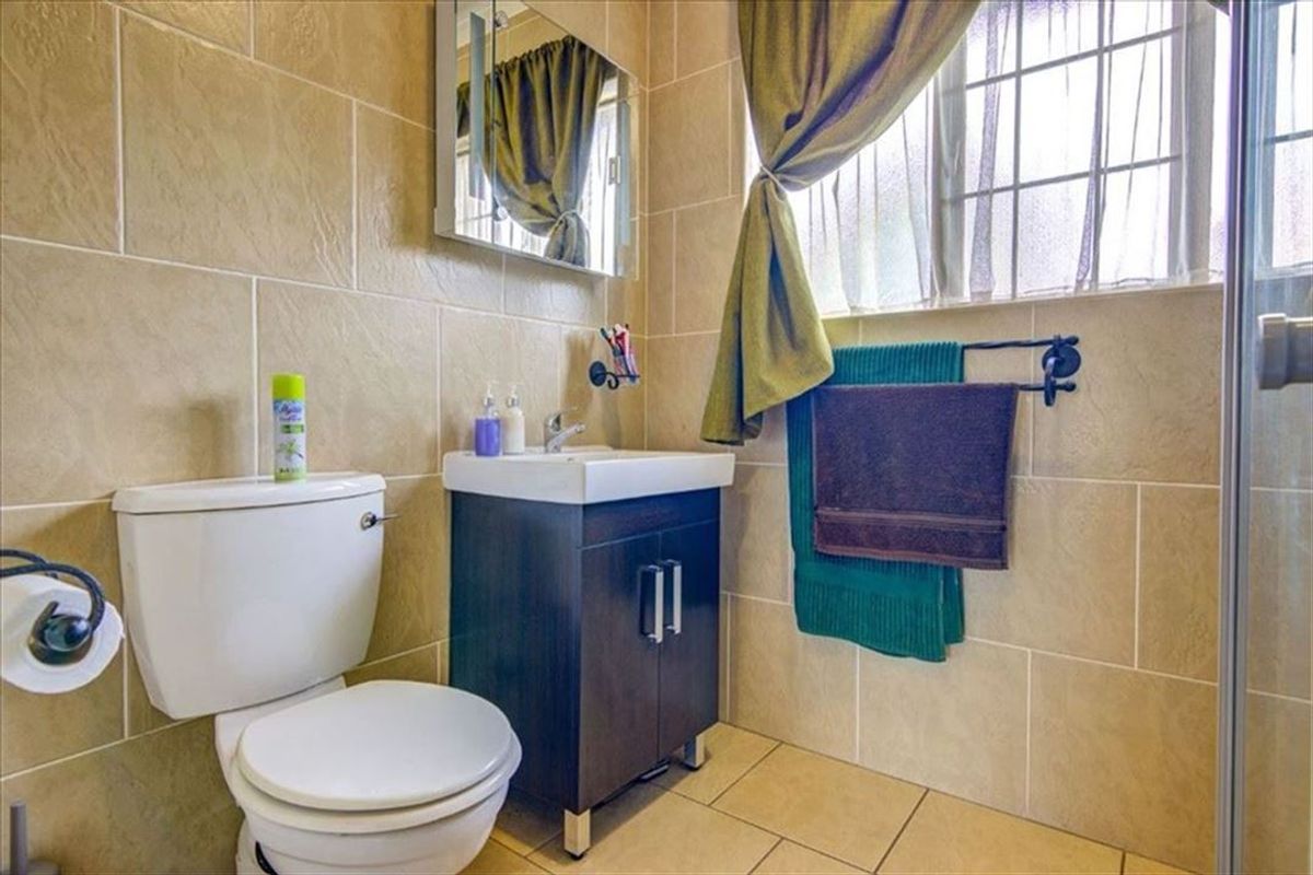A functional bathroom featuring a vanity cabinet with basin, toilet, and tiled finishes throughout, complemented by a window for natural light.