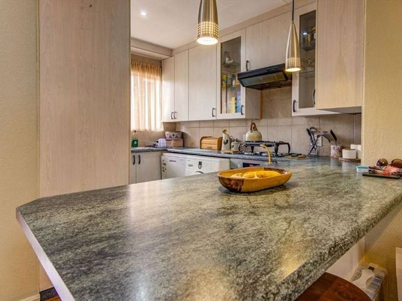 Functional kitchen featuring laminate cabinetry, stone-look countertops, a built-in gas hob with extractor fan, and a breakfast bar area.