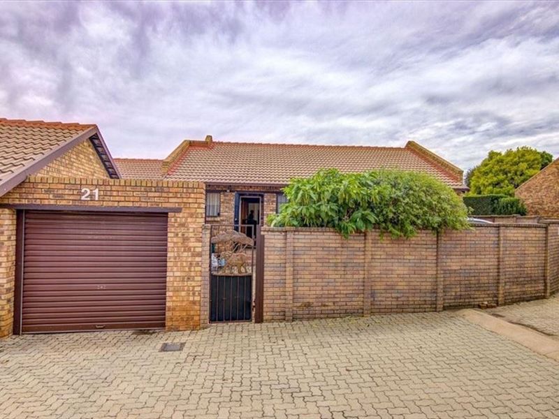 Front exterior view of a brick townhouse featuring a single garage, paved driveway, and a private gated entrance.