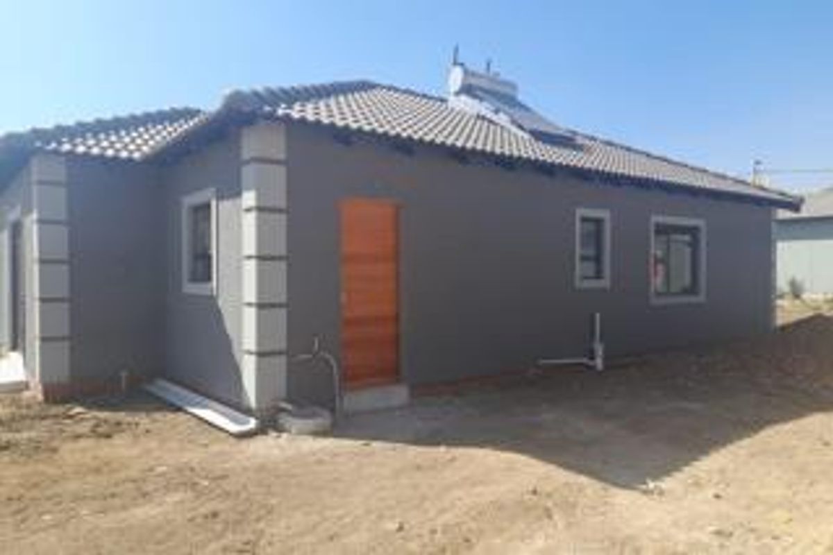 Rear view of a modern house featuring a tiled roof with a solar water heater and unfinished surrounding ground.