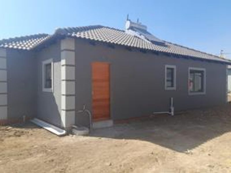 Rear view of a modern house featuring a tiled roof with a solar water heater and unfinished surrounding ground.