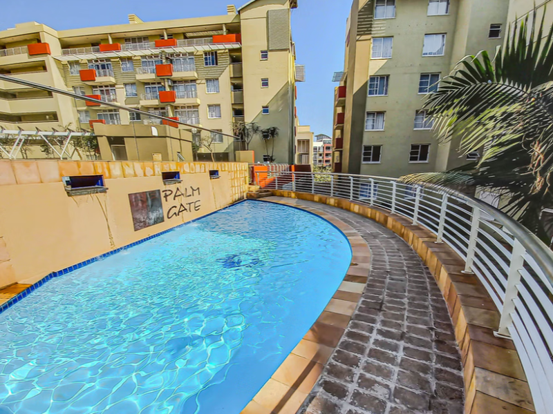 A communal swimming pool area featuring a curved stone-paved walkway, metal safety railings, and surrounding apartment building facades.