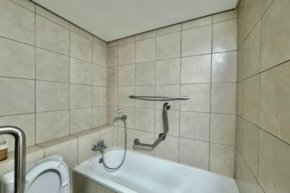 A functional bathroom featuring a bathtub with a shower mixer, tiled walls, and safety grab rails installed for accessibility.