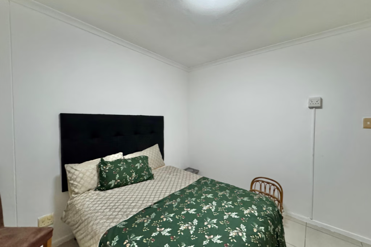 A simple bedroom featuring tiled flooring and white walls, with visible surface-mounted electrical wiring.