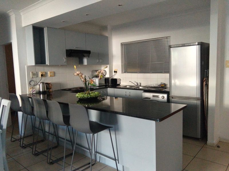 Modern kitchen featuring granite countertops, ample built-in cabinetry, a breakfast bar, and integrated appliances, finished with neutral tiled flooring.