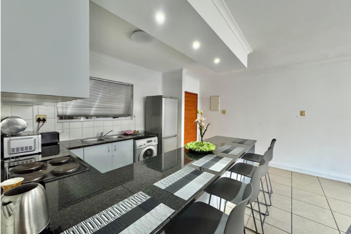 A functional kitchen featuring granite countertops, a built-in hob, double sink, and tiled flooring with an integrated breakfast bar area.