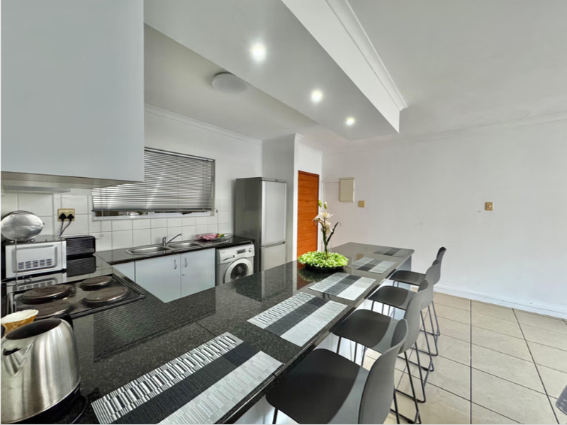 A functional kitchen featuring granite countertops, a built-in hob, double sink, and tiled flooring with an integrated breakfast bar area.